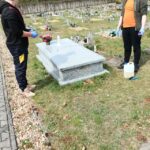 Cmentarz, wiele grobów przy jednym stoi dwóch nastolatków, którzy czyszczą pomnik